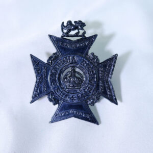The image shows a dark-toned metal cap badge for The Rhodesia Regiment, featuring a cross design with a central crown encircled by the regiment's name and campaign honours. The image shows a dark-toned metal cap badge for The Rhodesia Regiment, featuring a cross design with a central crown encircled by the regiment's name and campaign honours.