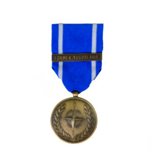miniature version of the NATO Medal for the Former Yugoslavia, featuring a bronze-finish circular medallion with the NATO star emblem surrounded by a wreath, suspended from a blue ribbon with white edge stripes and a 